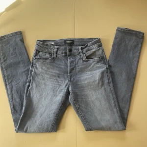 Slim Glenn grå jeans Jack & Jones - Inköpta i våras och i mycket bra skick. Slim Glenn jeans från Jack & Jones i ljusgrå tvätt med klassisk femficksdesign och snygga detaljer på bakfickorna. Modellen har smal passform och är tillverkad i mjukt jeanstyg med dragkedja och knappstängning. Perfekt för dig som gillar stilrena och moderna jeans.