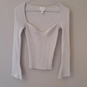 Ribbad ljusbeige topp från H&M - Säljer en ribbad ljusbeige långärmad topp från H&M med snygg v-ringning och figurnära passform. Toppen har markerade sömmar framtill som ger en cool look och är tillverkad i stretchigt material. Perfekt att styla med jeans eller kjol.