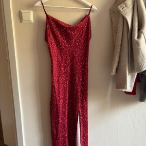 Röd prickig långklänning Paper Heart - Supersnygg röd långklänning från Paper Heart med vita prickar och smala axelband. Klänningen har en slits framtill och är gjord i ett glansigt, mjukt material som känns lyxigt. Perfekt för dig som vill sticka ut med en cool och trendig look. Har börjat slavad upp lite som visas i bilderna men borde vara lätt att fixa!