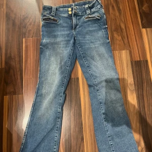 Blå bootcut jeans med dragkedjor - blå jeans med bootcut passform och coola dragkedjor vid fickorna framtill. Jeansen har dubbla knappar i midjan och klassiska bakfickor. Perfekta för dig som gillar en avslappnad men trendig stil.