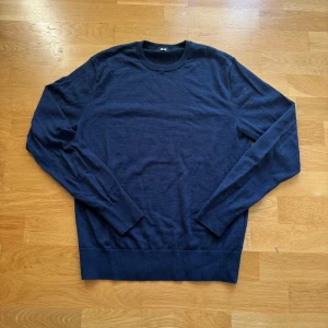 Mörkblå stickad tröja från Uniqlo - En stilren mörkblå stickad tröja från Uniqlo i storlek S. Tröjan har rund halsringning, långa ärmar och ribbade muddar vid ärmslut och nederkant. Perfekt för lager-på-lager och enkel att matcha med jeans eller chinos.