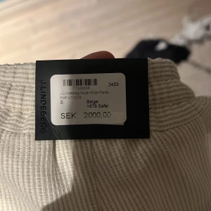 Beiga wide byxor från J.Lindeberg - Helt nya byxor från J.Lindeberg i modellen Noah Wide Pants. Byxorna har bred passform, elastisk midja med snörning och knapp, samt diskret struktur i tyget. Perfekta för semestrar i varmt klimat!!! Originalpris ligger på 2000 kr!!