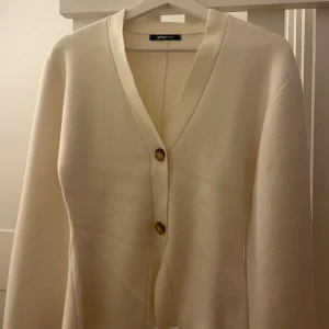 beige kofta från Gina Tricot - Superfin beige kofta från Gina Tricot med v-ringning och snygga knappar framtill. Koftan har lång ärm och är i mjukt material som känns skönt mot huden. Perfekt att slänga på sig när det är lite kyligt ute. 