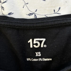 Svart långärmad topp från lager 157 XS - En stilren svart långärmad topp från lager 157 i storlek XS. Toppen har en enkel, klassisk design med rundad halsringning och är tillverkad i mjuk bomull med lite stretch för en bekväm passform. Perfekt att matcha med jeans eller kjol.