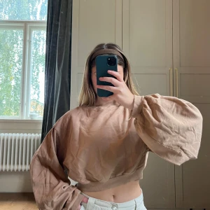 Beige croppad tröja med ballongärmar - Säljer en beige croppad tröja med breda ballongärmar och lös mudd i midjan och vid ärmslut. Tröjan har en loose passform.