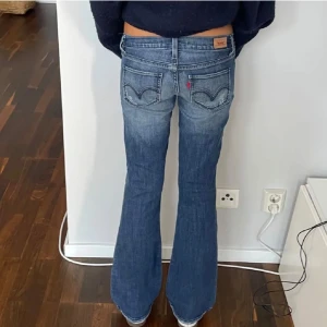 Levis  bootcut jeans blå - Snygga Levis 527 jeans i klassisk blå tvätt med bootcut passform och låg midja. Jeansen har fem fickor, tydliga slitningar och Levis ikoniska läderpatch bak. Perfekta för dig som gillar en avslappnad och trendig look.