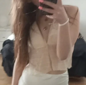 Beige croppad blus med v-ringning - Säljer en beige croppad blus med v-ringning och ärmlös design. Toppen har en lätt transparent look och knyts som en bekinitop, perfekt för dig som gillar en luftig och trendig stil.