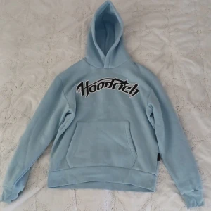 Ljusblå hoodie från Hoodrich XS - Säljer en ljusblå hoodie från Hoodrich i storlek XS. Tröjan har stor huva, magficka och Hoodrich-logga broderad i svart och vitt över bröstet. Perfekt för dig som gillar streetwear och vill ha en chill look.