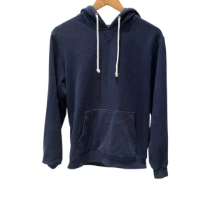 Mörkblå hoodie från Pier One - Mörkblå hoodie från Pier One med klassisk känguruficka och vita snören i huvan. Tröjan har lång ärm och är tillverkad i mjuk bomull, perfekt för chill dagar. Enkel och stilren design som funkar till det mesta.