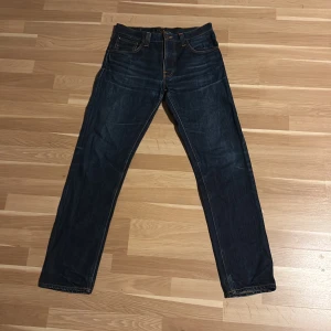 Mörkblå jeans från Nudie Jeans - Snygga mörkblå jeans från Nudie Jeans i storlek 33 34 med klassisk femficksdesign och kontrastsömmar. Jeansen har raka ben, tillverkade i slitstarkt denimtyg. Perfekta för dig som gillar stilrena och tidlösa jeans.