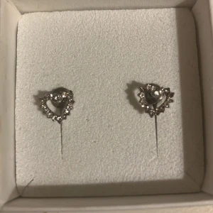 Hjärtformade silverörhängen med stenar - Säljer ett par söta örhängen i silverfärg, formade som hjärtan och dekorerade med gnistrande stenar runt kanten.