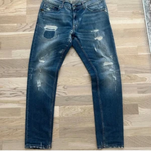 Tiger of Sweden slitna blå jeans - Blå jeans från Tiger of Sweden i modellen Evolve, med snygga slitningar och trasiga detaljer både fram och bak. Klassisk femficksmodell, tillverkade i Italien. Jeansen har en rak passform och coolt sliten look som ger en trendig vibe.