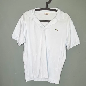 Ljus blåLacoste pikétröja i bomull - Ljus blåpikétröja från Lacoste med klassisk krage och korta ärmar. Ikoniska gröna krokodilloggan broderad på bröstet. Tillverkad i mjuk bomull för en skön och avslappnad stil. Perfekt för dig som gillar clean och sportig look. (Obs tröjan ser vit ut men är ljus blå!)