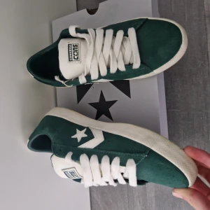 Gröna Converse sneakers i mocka - Säljer ett par gröna Converse sneakers med vit sula och vita detaljer. Skorna har snörning, rund tå och är tillverkade i mjuk mocka. Klassisk Converse-logga med stjärna på sidan och bak. Perfekt för dig som gillar retrostil och streetwear.