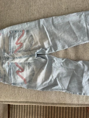 Ljusblå Nelly jeans - Säljer ett par ljusblå jeans med slitningar på knäna och broderade detaljer rosa . Hålen gjort av den ja köpte av super fina (ser bättre ut när dom sitter på) storlek 32