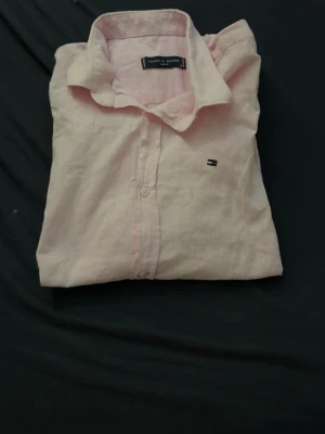 Storlek M men sitter som xs  - Säljer en stilren ljusrosa skjorta från Tommy Hilfiger med klassisk krage och knappstängning framtill. Skjortan har korta ärmar och den ikoniska lilla loggan broderad på bröstet. Perfekt för en fräsch och avslappnad look.