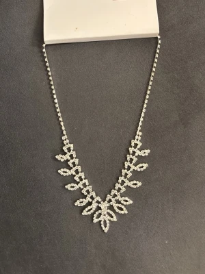 Glittrigt halsband med strassdetaljer - Ett snyggt halsband i silverfärg med glittrande strass i ett bladliknande mönster. Kedjan är tunn och dekorerad med små stenar hela vägen. Perfekt för att ge din outfit extra bling och wow-känsla.