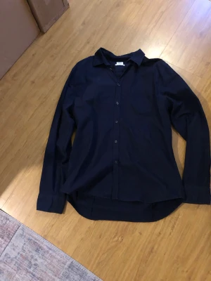 Mörkblå skjorta fillipa k - En stilren mörkblå skjorta med klassisk krage och knäppning framtill. Skjortan har lång ärm och en rak passform, perfekt för en clean och enkel look. Tillverkad i mjukt bomullstyg som känns skönt mot huden. Pris är inte bestämt.