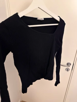 Svart ribbad långärmad topp - Säljer en svart ribbad långärmad topp med rund halsringning. Toppen har en tight passform och är tillverkad i ett stretchigt material som sitter snyggt på kroppen. Perfekt att matcha med jeans eller kjol för en clean look. Jag har vanligt vis storlek S och passar mig perfekt 
