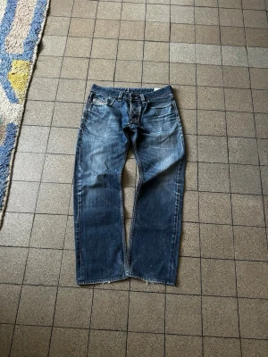 Mörkblå diesel larkee - Säljer ett par klassiska blå jeans med raka ben och snygga slitningar framtill. Jeansen har fem fickor, normal midja och kontrastsömmar. Perfekta för en avslappnad och trendig look. Materialet är denim i bomull. Gjorda i Italien, snygg distressing och tvätt.