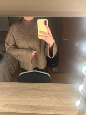 Brun kabelstickad oversized tröja - Mysig brun kabelstickad tröja med oversized passform och höga, vida ärmar. Tröjan har ribbad mudd vid hals, ärmslut och nederkant. Perfekt för lager-på-lager och chill dagar.