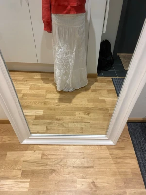 Vit lång boho-kjol med resårmidja - Säljer en vit långkjol i boho-stil med bred resår i midjan och volangdetaljer. Kjolen är luftig och har ett skirt, lätt material som ger ett avslappnat intryck. Perfekt för dig som gillar en enkel men trendig look.