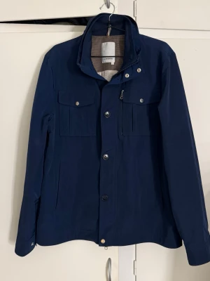 J.Lindeberg jacka - En stilren och modern J.Lindeberg-jacka i en elegant mörkblå färg. Ett kvalitativt ytterplagg med minimalistisk design och hög komfort, perfekt för dig som vill ha en jacka som fungerar lika bra till vardag som till mer uppklädda tillfällen. Idealisk för vårsäsongen.  ✅ Märke: J.Lindeberg ✅ Storlek: L ✅ Färg: Mörkblå ✅ Skick: Använd men i mycket bra skick ✅ Passform & känsla: Lätt och bekväm, perfekt för våren  En snygg och mångsidig vårjacka från J.Lindeberg – redo att användas direkt.