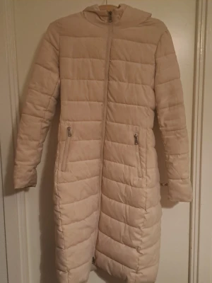 Lång dunjacka med fuskpälskrage - Har luva och fickor. Hittar inga defekter förutom en fläck på baksidan och ena ärmen, men går säkert bort efter en tvätt. Finns en krage i vit fuskpäls till som man fäster runt nacken. 🩷