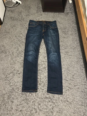 Mörkblå jeans från Nudie Jeans - Snygga mörkblå jeans från Nudie Jeans med klassisk femficksmodell och kontrastsömmar🔥Jeansen har raka ben och är tillverkade i slitstark denim med coola slitningar på låren👌Perfekta för en avslappnad och trendig stil.