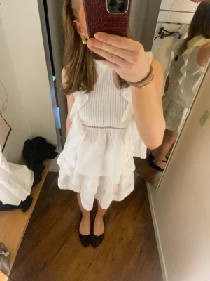 Vit volang topp och kjol från BikBok - Supersöt vit kjol och topp med volanger. Klänningen har ribbad överdel och flera lager volanger i kjolen, vilket ger en luftig och trendig look. Perfekt för varma dagar och somriga tillfällen. Även bra till studenten eller skolavslutning. S i kjolen och L i toppen. Skriv för fler bilder. 