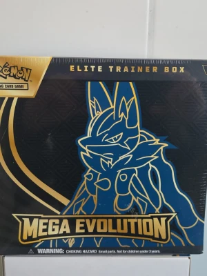 Pokémon Mega Evolution Elite Trainer Box - Säljer en Pokémon Mega Evolution Elite Trainer Box med motiv av Lucario i blått och guld. Boxen innehåller booster packs, promokort, energikort, tärningar och samlartillbehör. Perfekt för dig som vill ta ditt Pokémon TCG-spelande till nästa nivå.