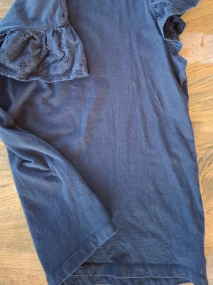 Svart topp med volangärm - Svart topp med korta volangärmar i broderad bomull. Ärmarna har fina spetsdetaljer och ger en söt touch till toppen. 