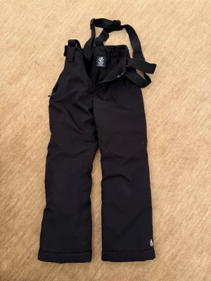 Svarta skidbyxor med hängslen - Säljer ett par svarta skidbyxor från Dare2B med justerbara hängslen och dragkedja fram. Byxorna har raka ben och är tillverkade i slitstarkt, vattenavvisande material. Perfekta för kalla dagar i backen eller snölek.