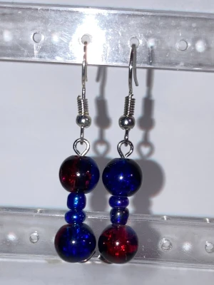 Blå och röda pärlörhängen - Unika handgjorda örhängen med pärlor i blått och rött. Örhängena har två större glaspärlor i djupa färger och två mindre blå pärlor på varje örhänge. Krokar i silverfärgad metall. Perfekta för dig som vill sticka ut med färg och personlighet.