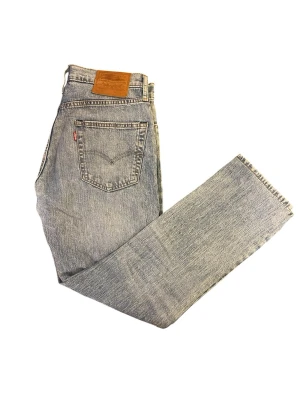 Levi's 501 ljusblå raka jeans 30 32 - Klassiska Levi's 501 jeans i ljusblå tvätt med rak passform och hög midja. Jeansen har fem fickor, knappgylf och den ikoniska läderlappen bak i midjan. Tillverkade i slitstark bomull med vintagekänsla och subtila slitningar för en avslappnad look.