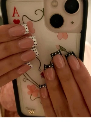 Press-on naglar med prickig fransk tipp - Snygga press-on naglar med fransk tipp i svart och vitt med prickigt mönster. Naglarna har en fyrkantig form och en naturligt nude bas. Perfekt för dig som vill ha en trendig och lekfull look. Materialet är plast.