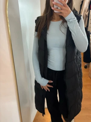 Zara Svart lång dunväst  - Säljer en svart lång dunväst från Zara. Västen är vattenavvisande, vindtät, lätt och andas. Perfekt för lager-på-lager och har en clean, stilren look med quiltad design. Nypris: 1 000 kr. Spegeln är fläckig själva jackan är felfri.