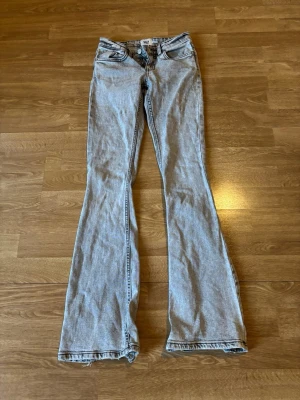 Ljusgrå bootcut jeans från Lager157 - Säljer ett par ljusgrå bootcut jeans från Lager157 med klassisk femficksdesign och låg midja. Jeansen har utsvängda ben och råa kanter nertill för en cool och avslappnad look. Perfekta för dig som gillar retrostil och vill sticka ut.