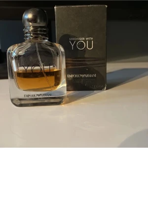 Emporio Armani Stronger With You parfym - Emporio Armani Stronger With You är en elegant parfym i en genomskinlig glasflaska med rundad form och svart metallkork. Doften har en varm bärnstensfärgad vätska och kommer i en stilren svart förpackning med silverdetaljer.