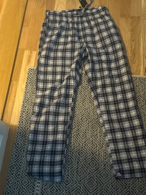 Rutiga pyjamasbyxor från 157 - Mysiga pyjamasbyxor från 157 i blåvitt rutigt mönster. Byxorna har resår i midjan och dragsko för extra komfort. Perfekta för chillkvällar hemma. Tillverkade i mjukt tyg som känns skönt mot huden.