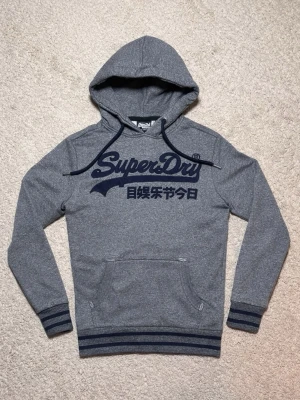Superdry Hoodie - Grå Superdry Hoodie - Storlek: S - Pris: 599kr - Tröjan är i fint skick utan defekter - Först till kvarn! 