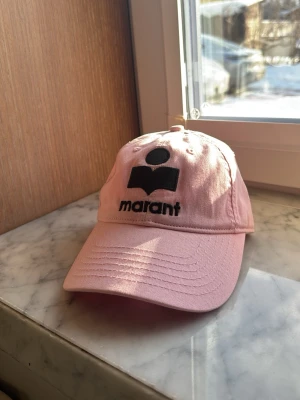 Rosa keps från Marant - Snygg rosa keps från Marant med svart broderad logga och text framtill. Klassisk böjd skärm och justerbar passform bak. Jätte skön att ha på sig och passar perfekt till sommaren om du gillar färg! Säljer för att den tyvärr inte kommit till användning .