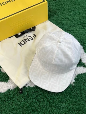 Vit keps med FF-mönster från Fendi - Säljer en stilren vit keps från Fendi med det klassiska FF-monogrammet ton-i-ton över hela kepsen. Kepsen har böjd skärm och justerbar baksida. Materialet ser ut att vara bomull eller en bomullsblandning. Perfekt för dig som gillar exklusiva accessoarer.