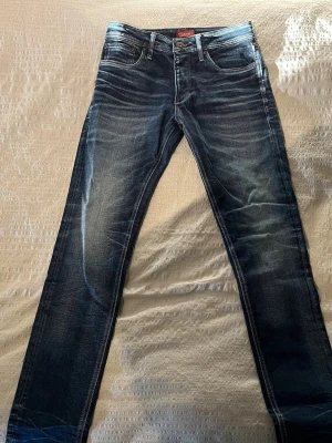 Mörkblå jeans från Jack & Jones - Snygga mörkblå jeans från Jack & Jones med slitna detaljer och kontrastsömmar. Modellen har klassisk femficksdesign, raka ben och läderpatch bak i midjan. Stilrena med en washed finish. 