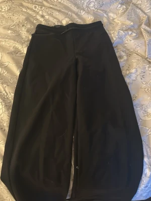 Svarta mjukisbyxor med dragsko - Ett par svarta mjukisbyxor med avslappnad passform och dragsko i midjan. Tillverkade i mjukt och stretchigt material som gör dem riktigt sköna att ha på sig. Perfekta för chill eller när du vill vara bekväm hela dagen.