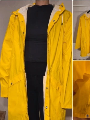 Gul regnjacka från RAINS - Snygg gul regnjacka från RAINS med huva och vita dragskor. Jackan har tryckknappar framtill, fickor med lock och är tillverkad i ett vattenavvisande material. Perfekt för regniga dagar och ger en färgklick till din outfit.