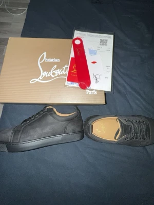 Svarta sneakers från Christian Louboutin - Säljer ett par svarta sneakers från Christian Louboutin med klassisk design och diskret logga på innersulan. Skorna har svarta skosnören, svart sula och är tillverkade i mocka. Kommer med originalkartong och tillbehör. Pris diskuteras privat.