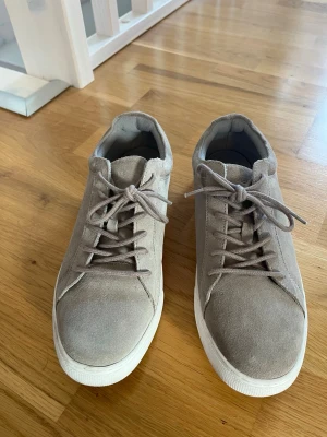 Beige sneakers från Jack & Jones - Stilrena beige sneakers från Jack & Jones i mocka med vita sulor. Klassisk låg modell med snörning och diskret logga på sidan. Perfekta för en clean och avslappnad look. Använd en gång.