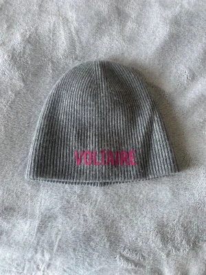Grå ribbstickad mössa Voltaire - Grå ribbstickad mössa från Voltaire med rosa broderad logga framtill. Inte alls använd och väldigt varm och skön