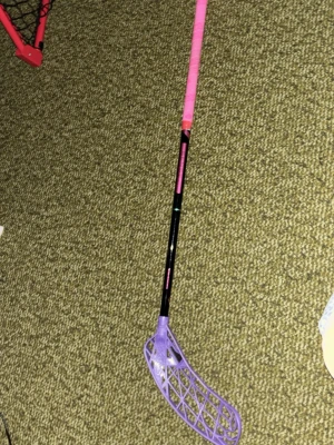 Innebandyklubba med lila blad - Säljer en innebandyklubba med svart skaft, rosa grepp och ett lila plastblad. Perfekt för dig som gillar färgglada sportprylar. Klubban har ett greppvänligt handtag och ett blad med öppen struktur för bra bollkontroll.